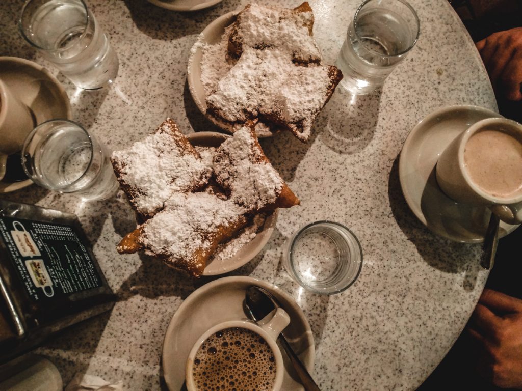 Chicory coffee (cafe au lait) at Cafe Du Monde in New Orleans. Glasses of water. Powdered sugar beignets. 
