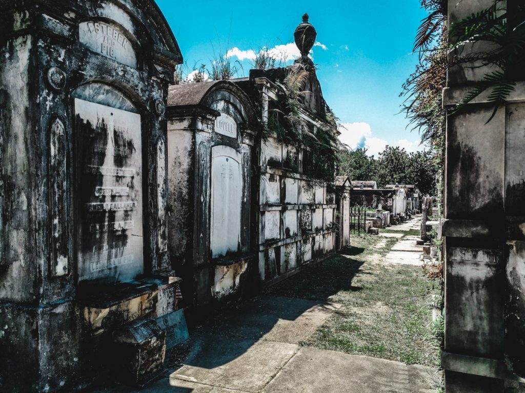 Weathered, old family tombs in New Orleans Layafette Cemetery. Bright blue sky.